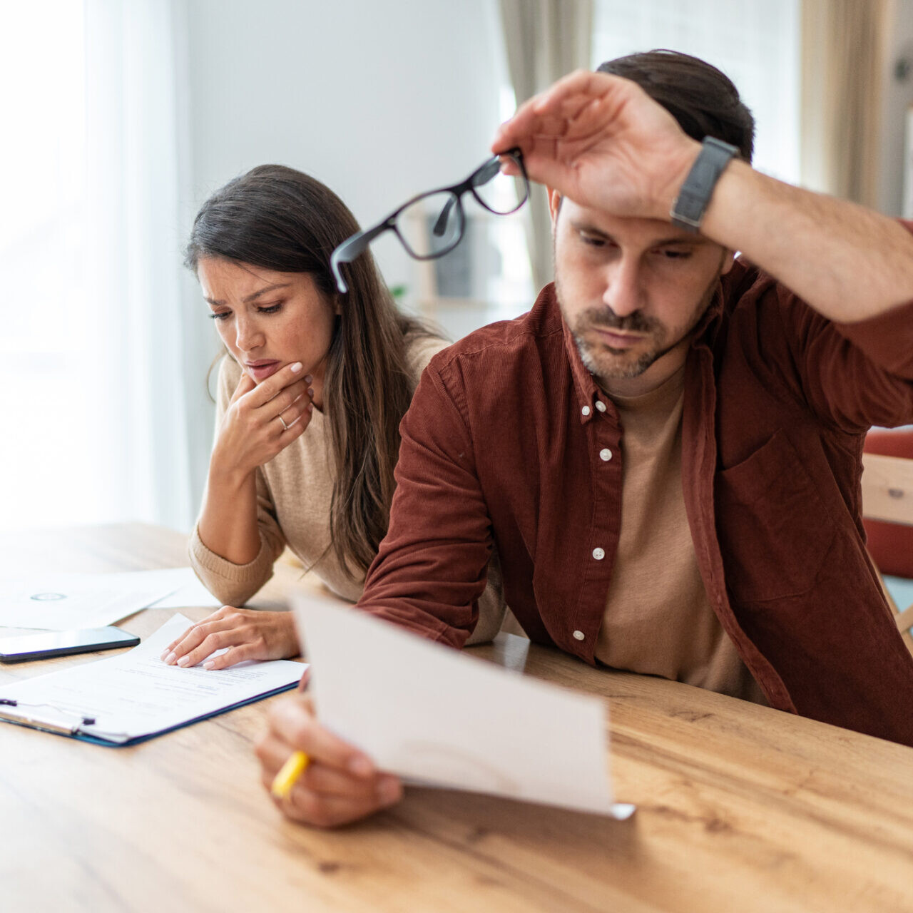 Couple inquiet examinant des documents financiers à la maison, illustrant une situation de surendettement.