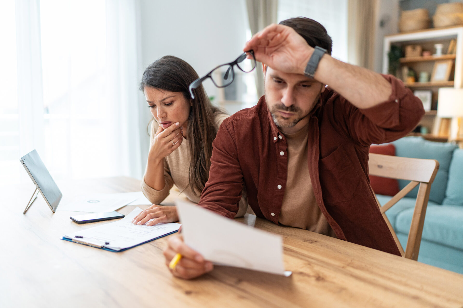 Couple inquiet examinant des documents financiers à la maison, illustrant une situation de surendettement.