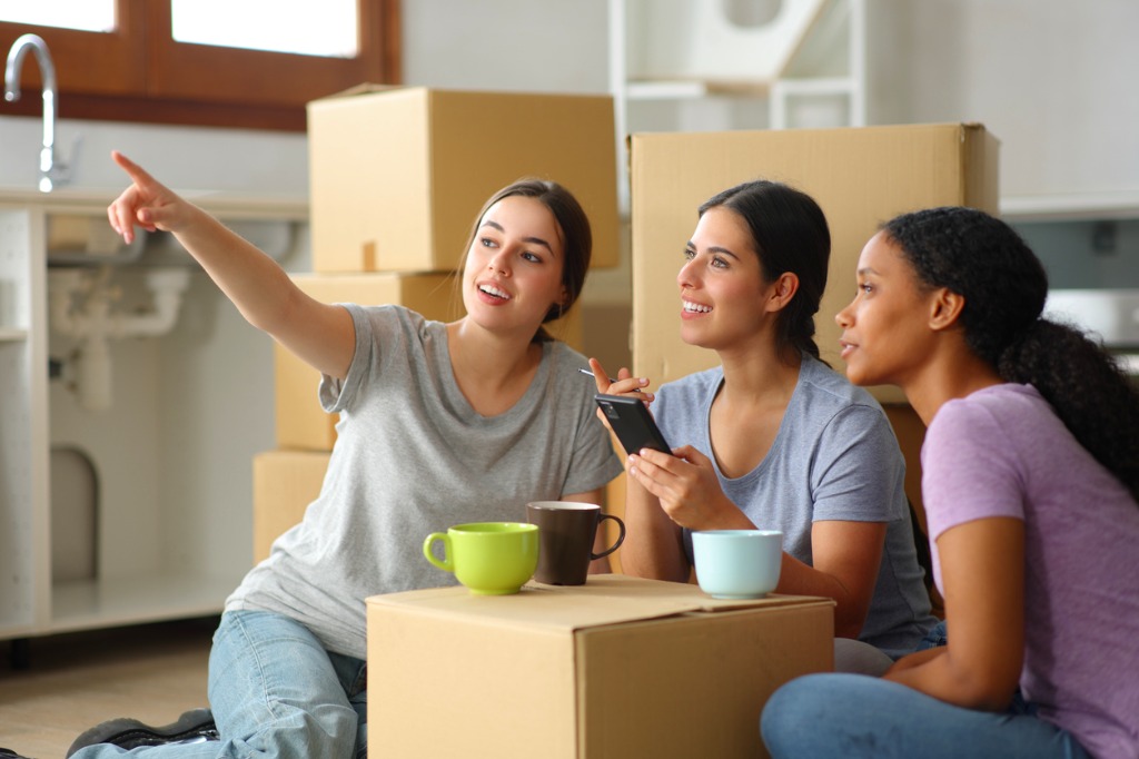Trois jeunes femmes en colocation assises au sol, entourées de boîtes de déménagement, dans une ambiance conviviale.