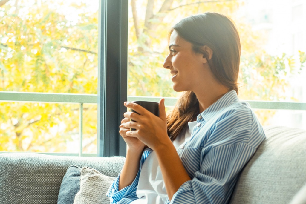 Femme détendue à la maison, illustrant la réflexion : est-ce que l’argent fait le bonheur dans une vie simple.