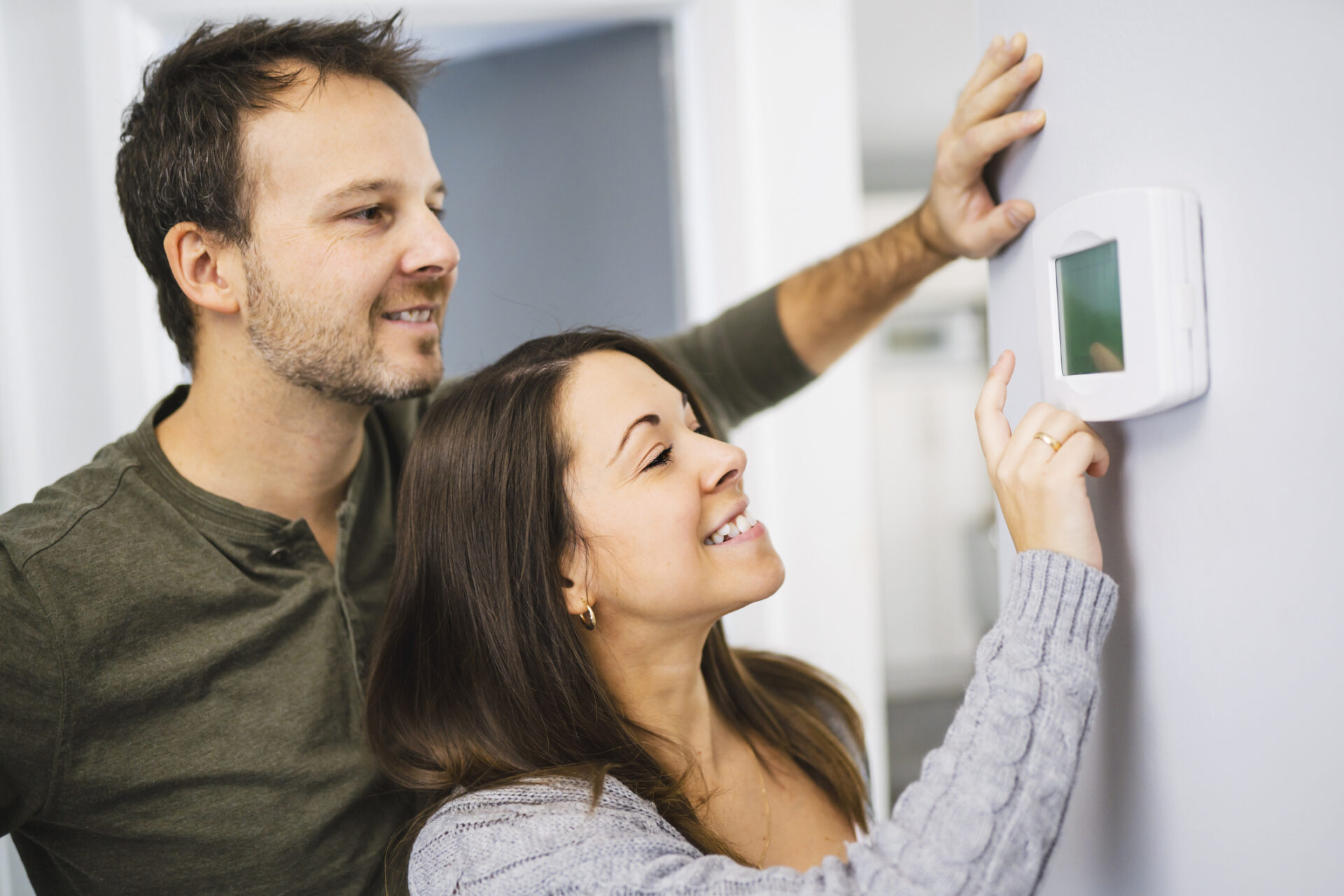 Couple ajustant un thermostat pour réduire les factures d’énergie à la maison.