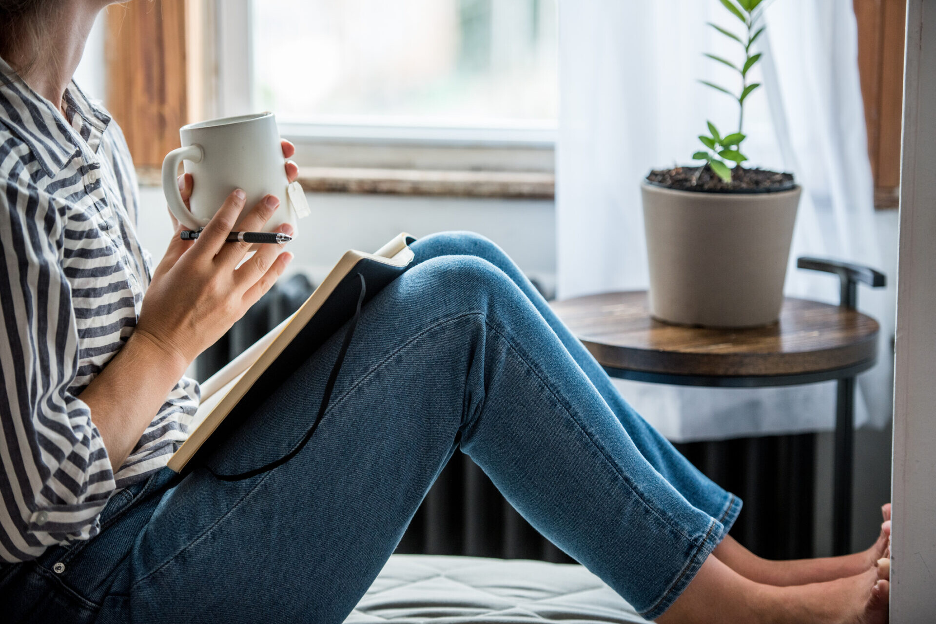 Femme en pleine réflexion avec un carnet et une tasse de thé, illustrant le concept d’investir en soi à la maison.