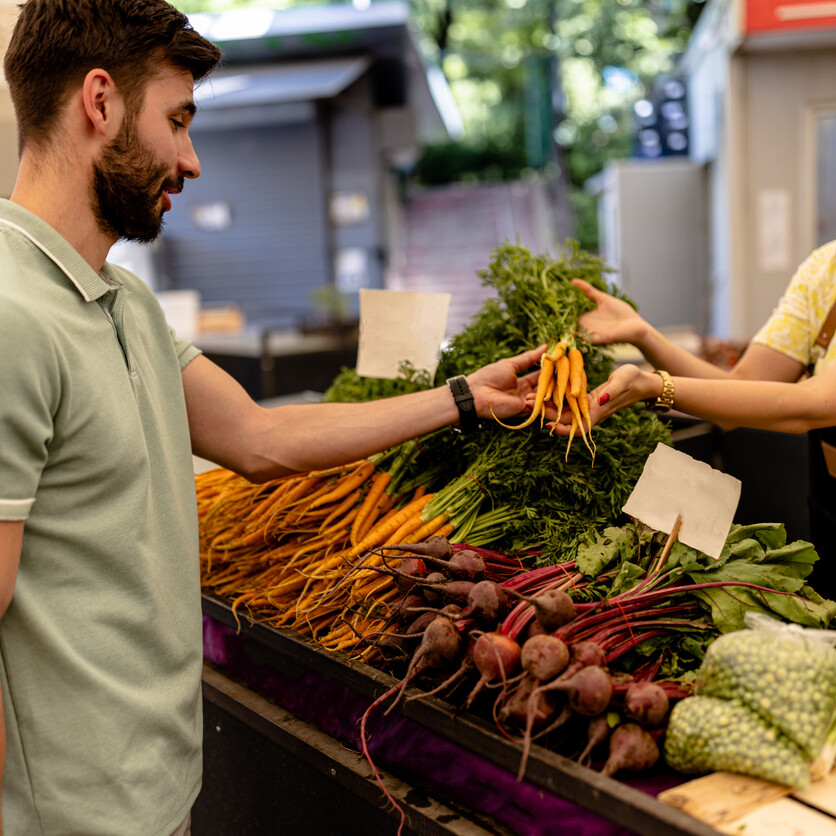 Achat local au marché : un homme choisit des légumes frais auprès d’une productrice locale au Québec.