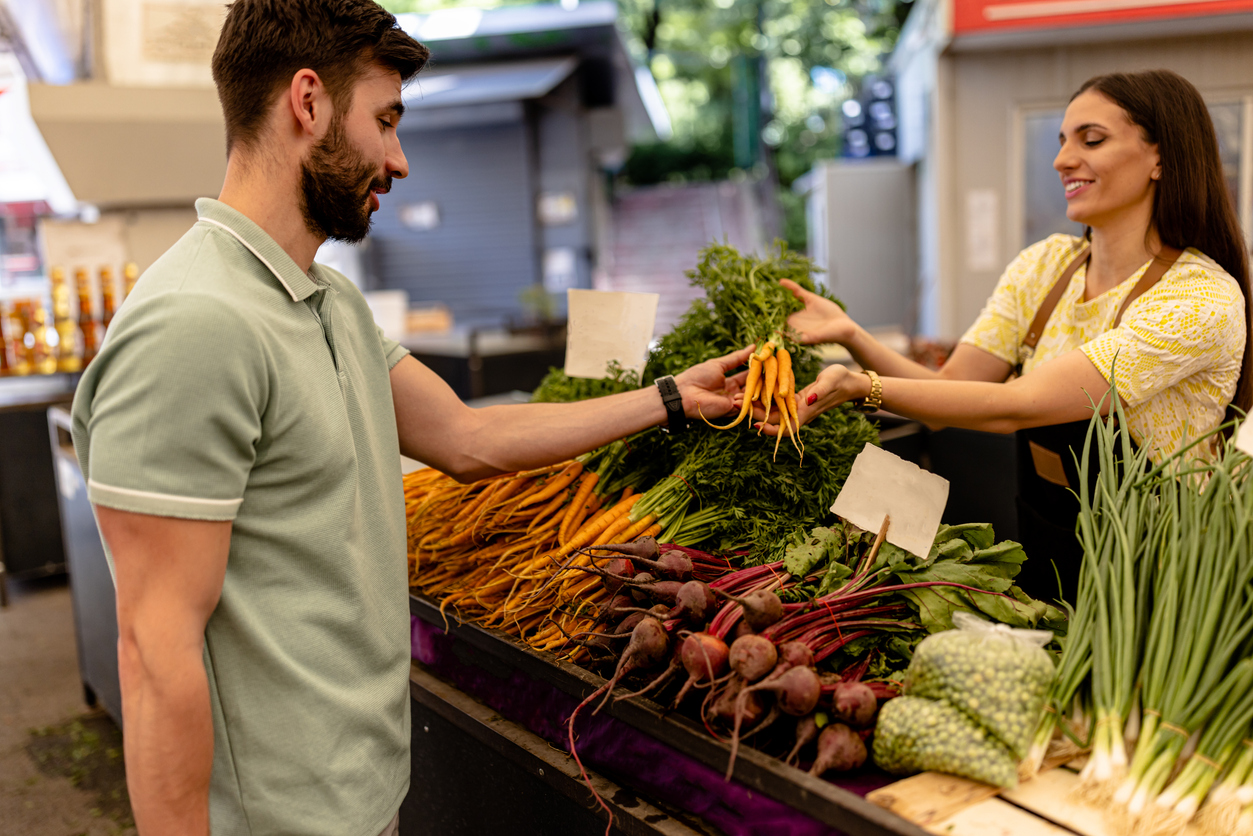 Achat local au marché : un homme choisit des légumes frais auprès d’une productrice locale au Québec.