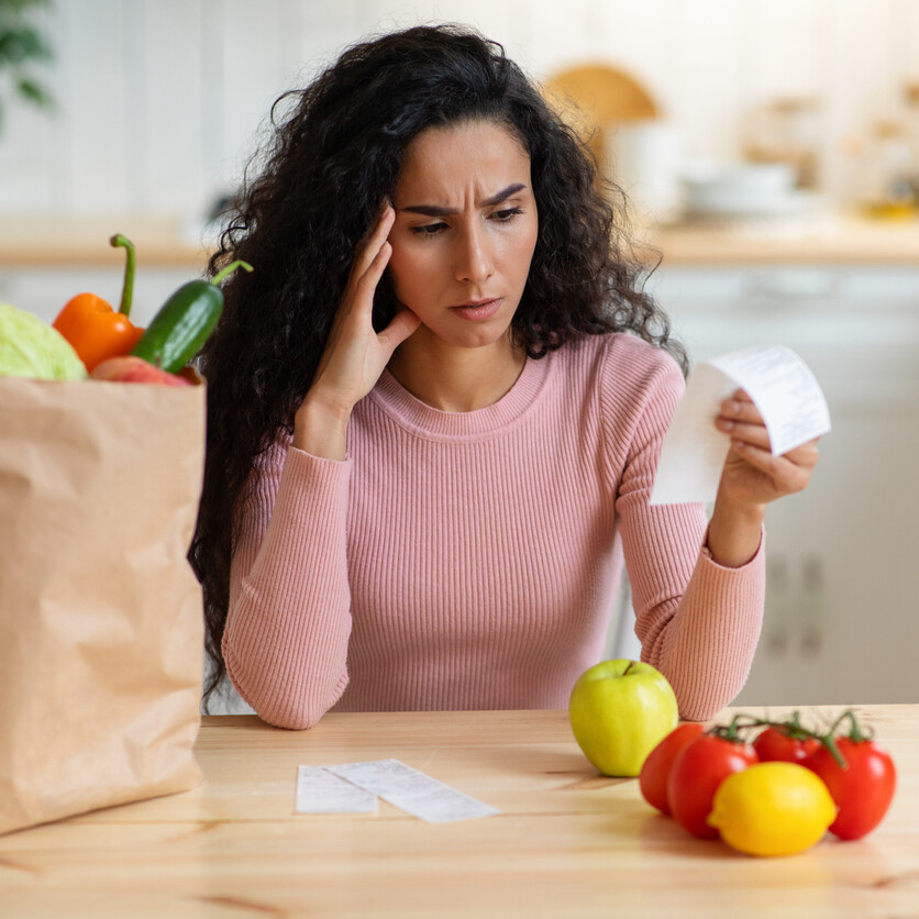 Femme inquiète examinant facture d'épicerie, reflétant l'impact de l'inflation sur le budget.