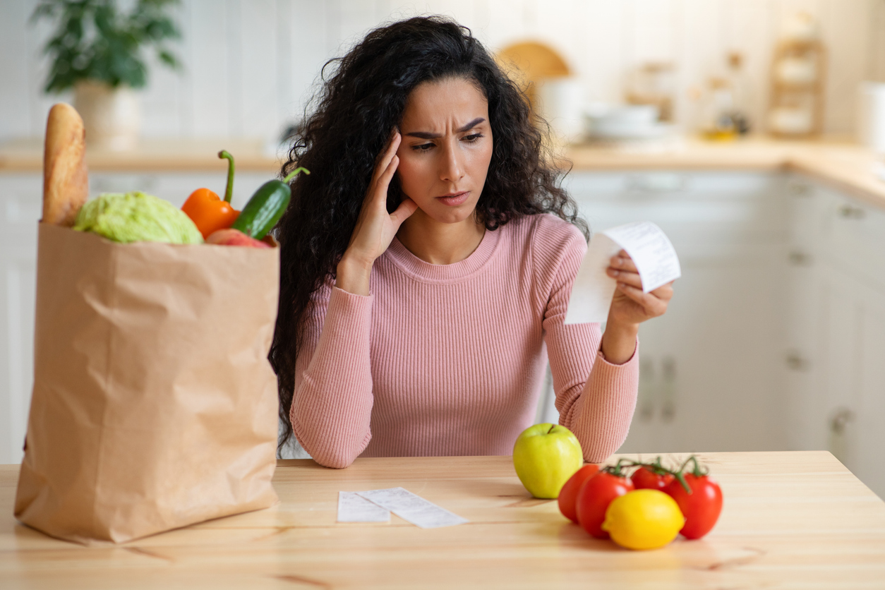 Femme inquiète examinant facture d'épicerie, reflétant l'impact de l'inflation sur le budget.