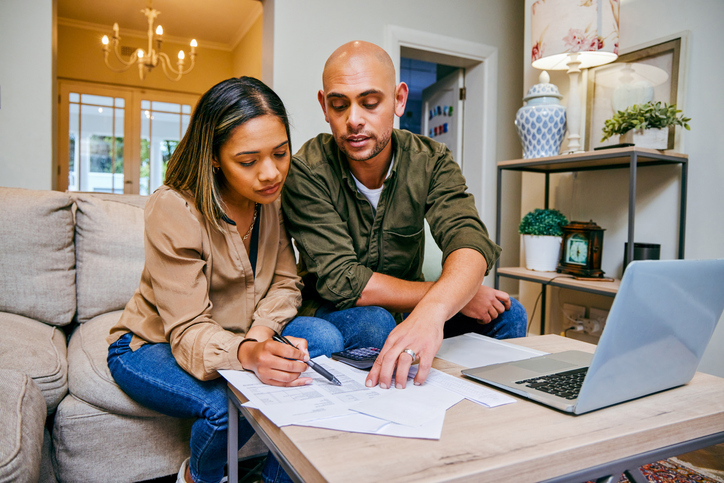 Couple à la maison examinant des documents pour réduire le coût des assurances. avec un ordinateur portable.