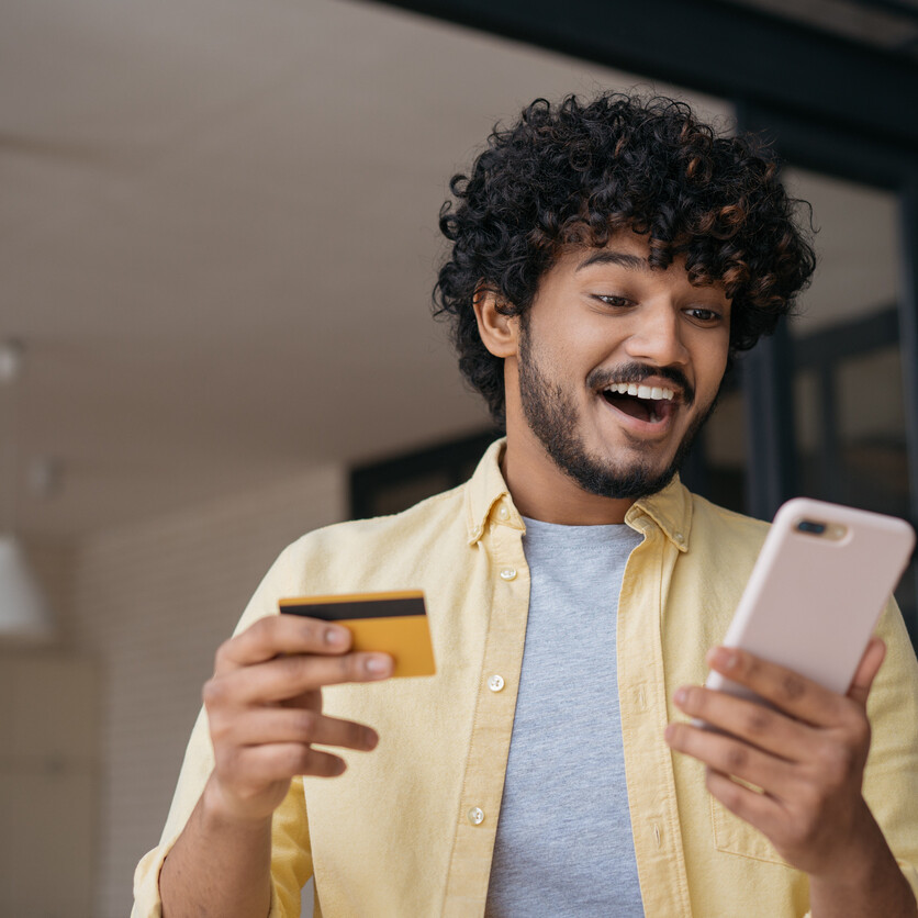 Jeune adulte découvrant des avantages grâce à sa carte de crédit à récompenses sur son téléphone.