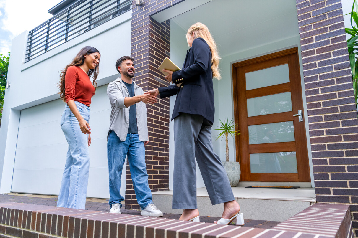 Couple rencontrant un agent immobilier devant une maison, illustrant la décision de louer ou acheter une maison.