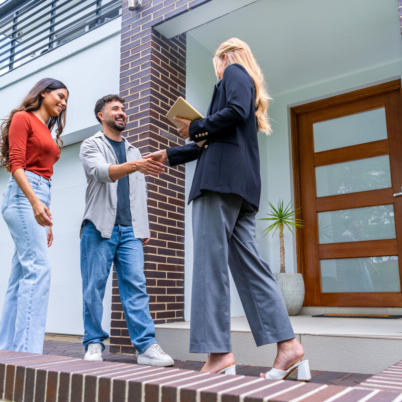 Couple rencontrant un agent immobilier devant une maison, illustrant la décision de louer ou acheter une maison.