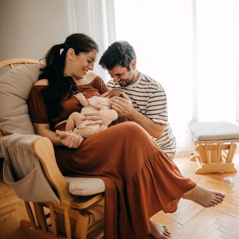 Jeunes parents en congé parental tenant leur bébé dans une ambiance chaleureuse à la maison.