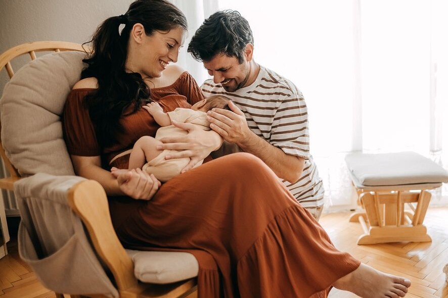 Jeunes parents en congé parental tenant leur bébé dans une ambiance chaleureuse à la maison.